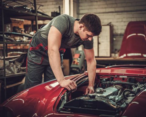 A young male mechanic in a restoration workshop working on a classic car with an electric powertrain.