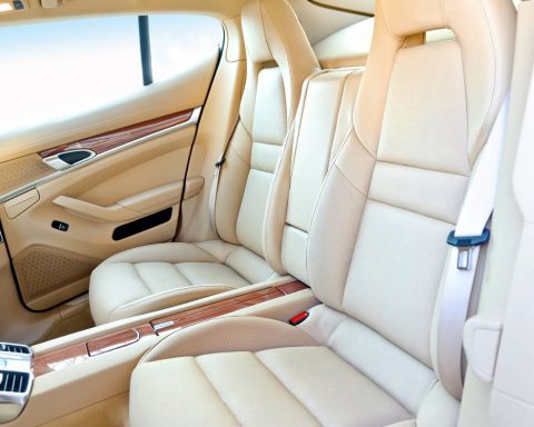 The interior of a luxury vehicle showing the cream colored rear leather seats, middle console, and back door.