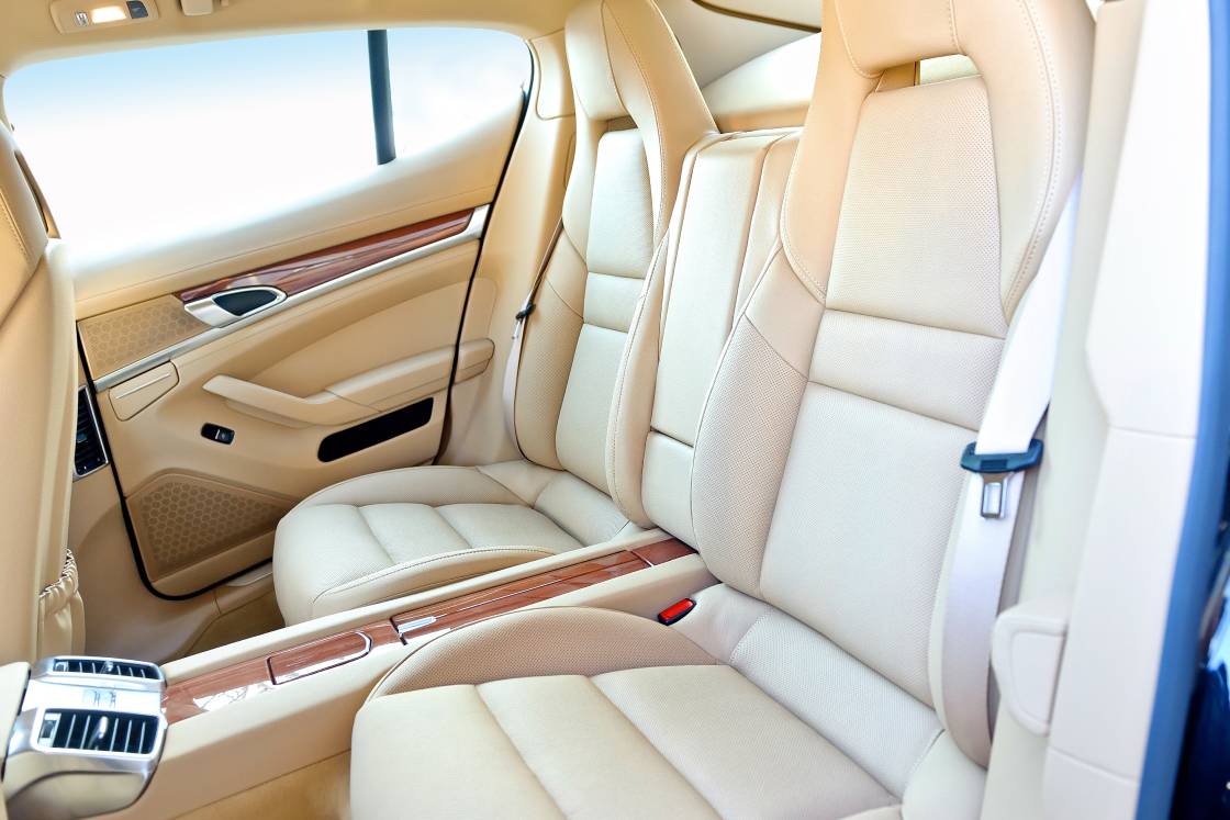 The interior of a luxury vehicle showing the cream colored rear leather seats, middle console, and back door.
