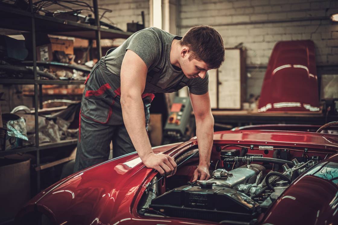 A young male mechanic in a restoration workshop working on a classic car with an electric powertrain.