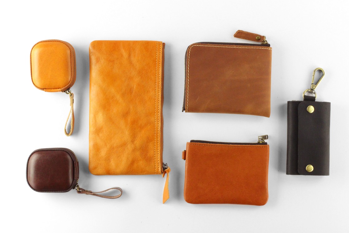An assortment of leather pouches and wallets, ranging in color from light brown to almost black, against a white background.